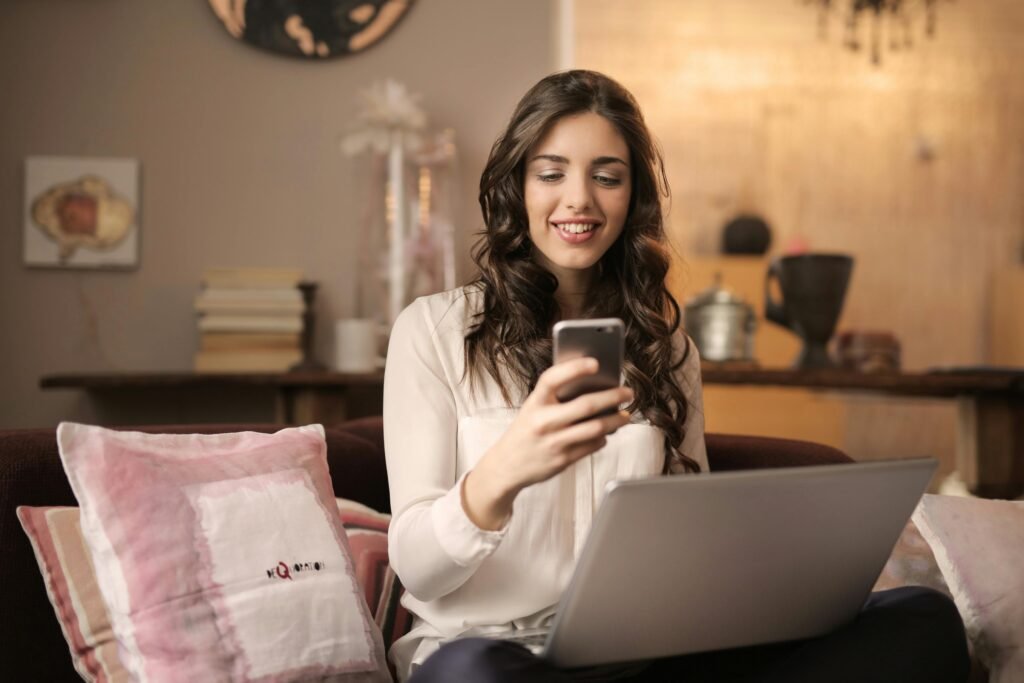 Beauty blog A woman enjoying leisure time using her smartphone and laptop in a cozy living room.